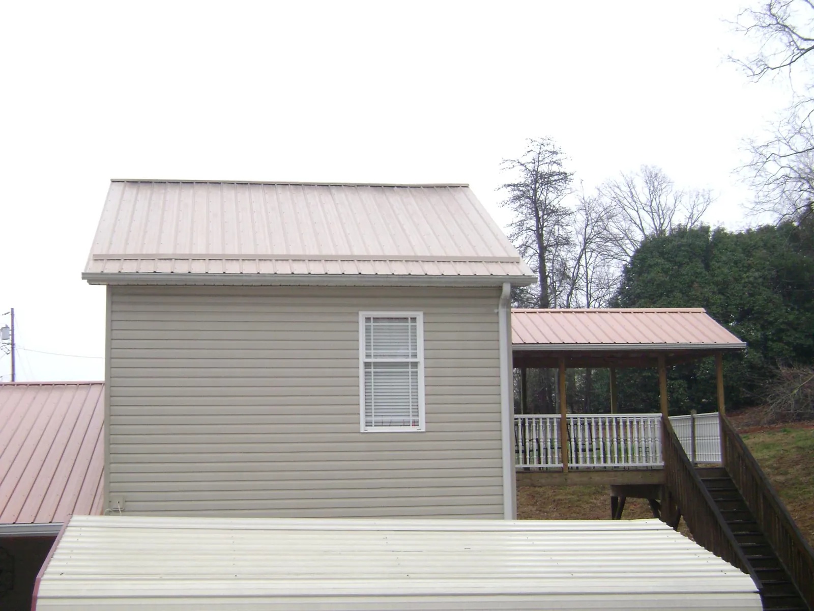 Tan metal roofs on a two story addition and attached porch, from a Roof Replacement job in Commerce